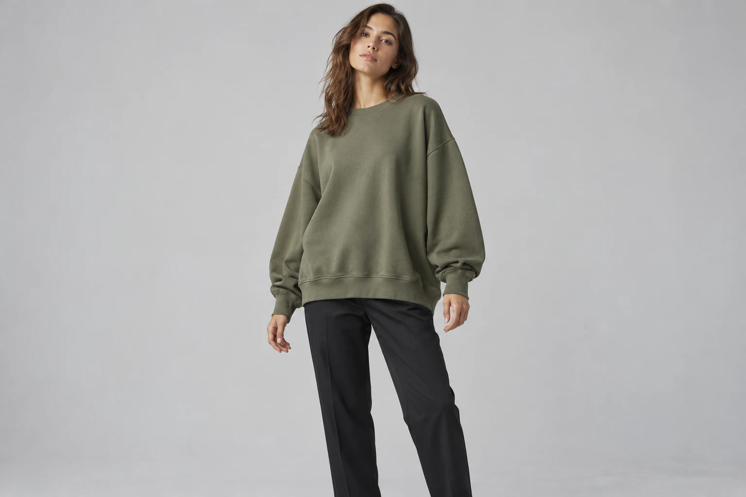 Conceptual lookbook photograph of an adult model wearing a roomy olive sweatshirt with dropped shoulders and visible cuffs